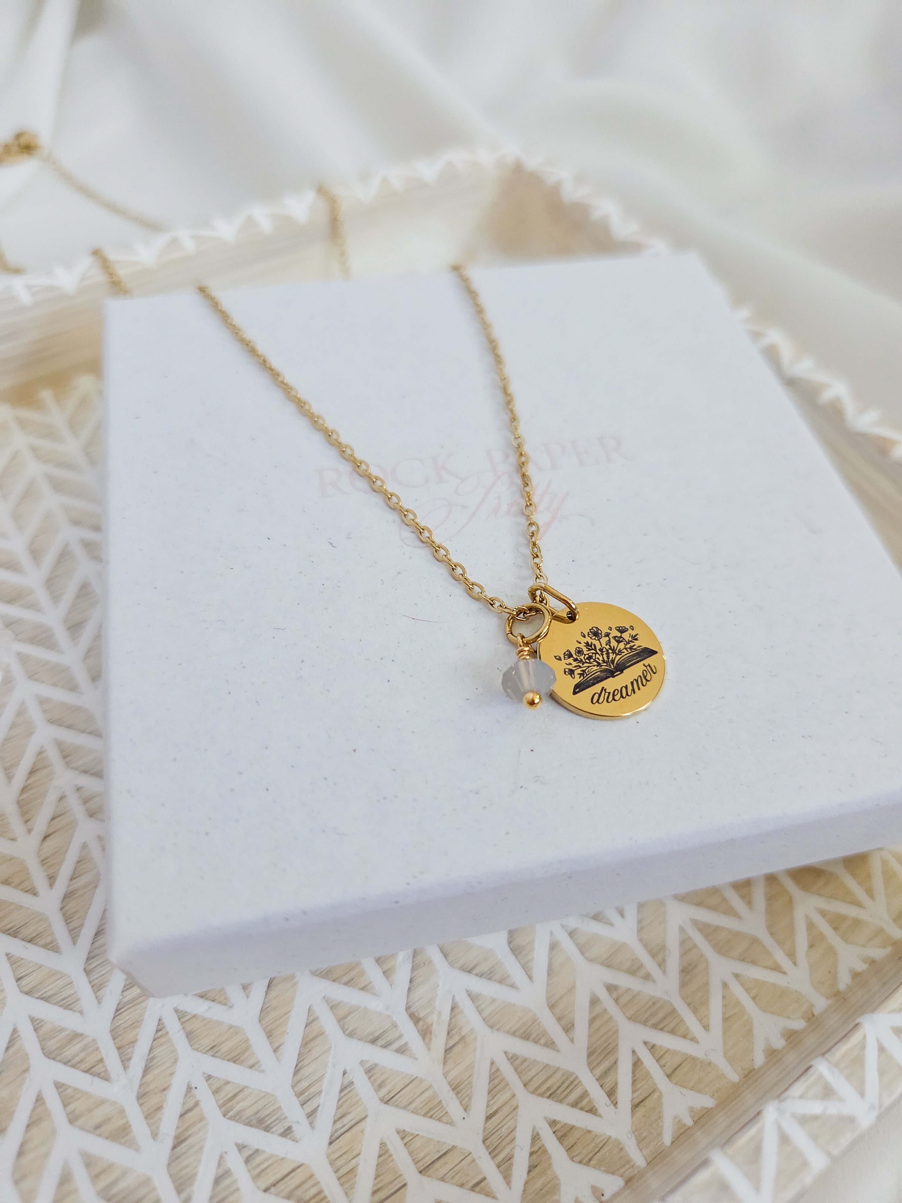 Gold necklace with a gold disc pendant on a white jewelry box. Waterproof necklace for book lovers.