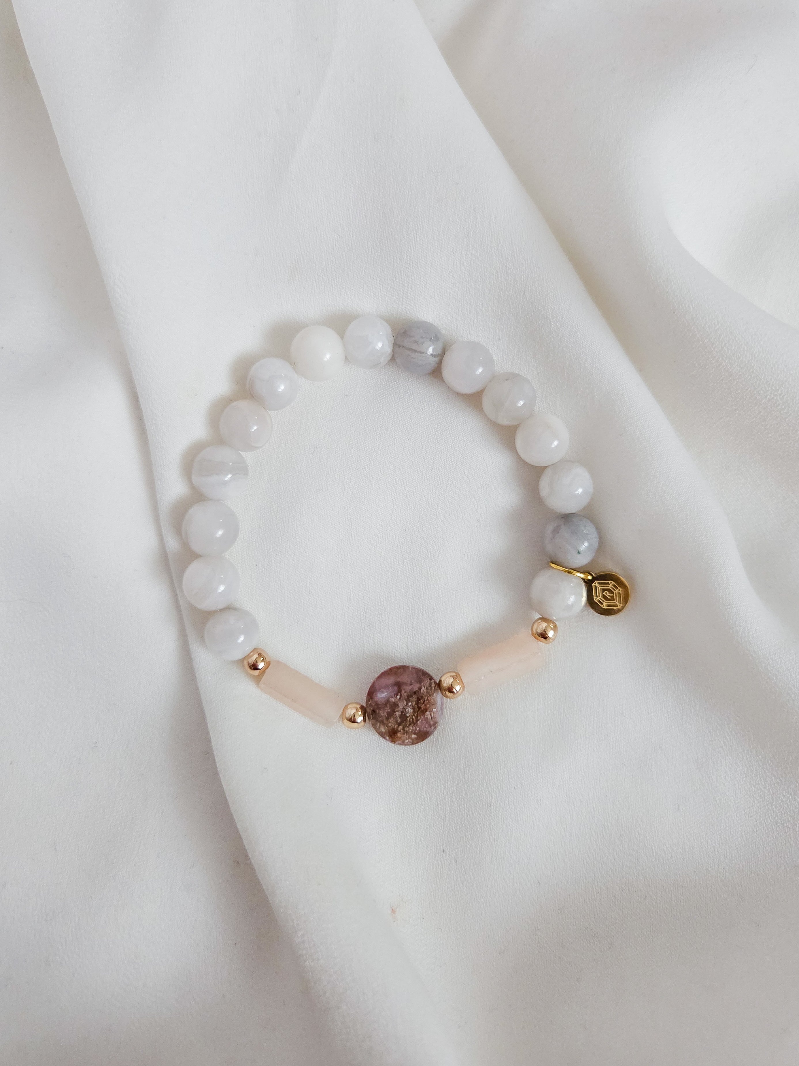 Bracelet with white lace agate, pink aventurine and fire agate gemstone beads on a white fabric background