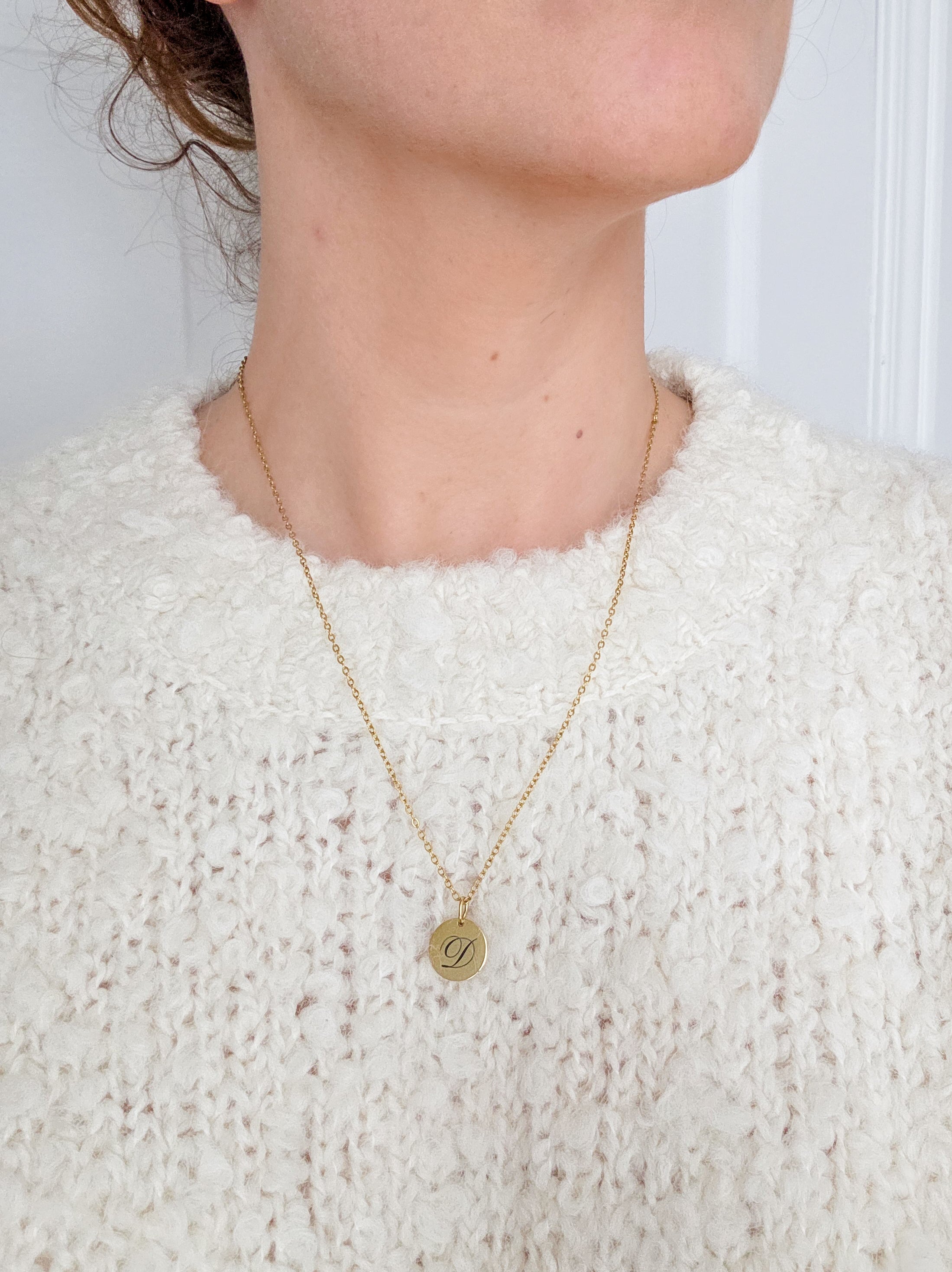 Gold necklace with a round pendant worn by a person in a white textured sweater. Gold necklace with Initial pendant.