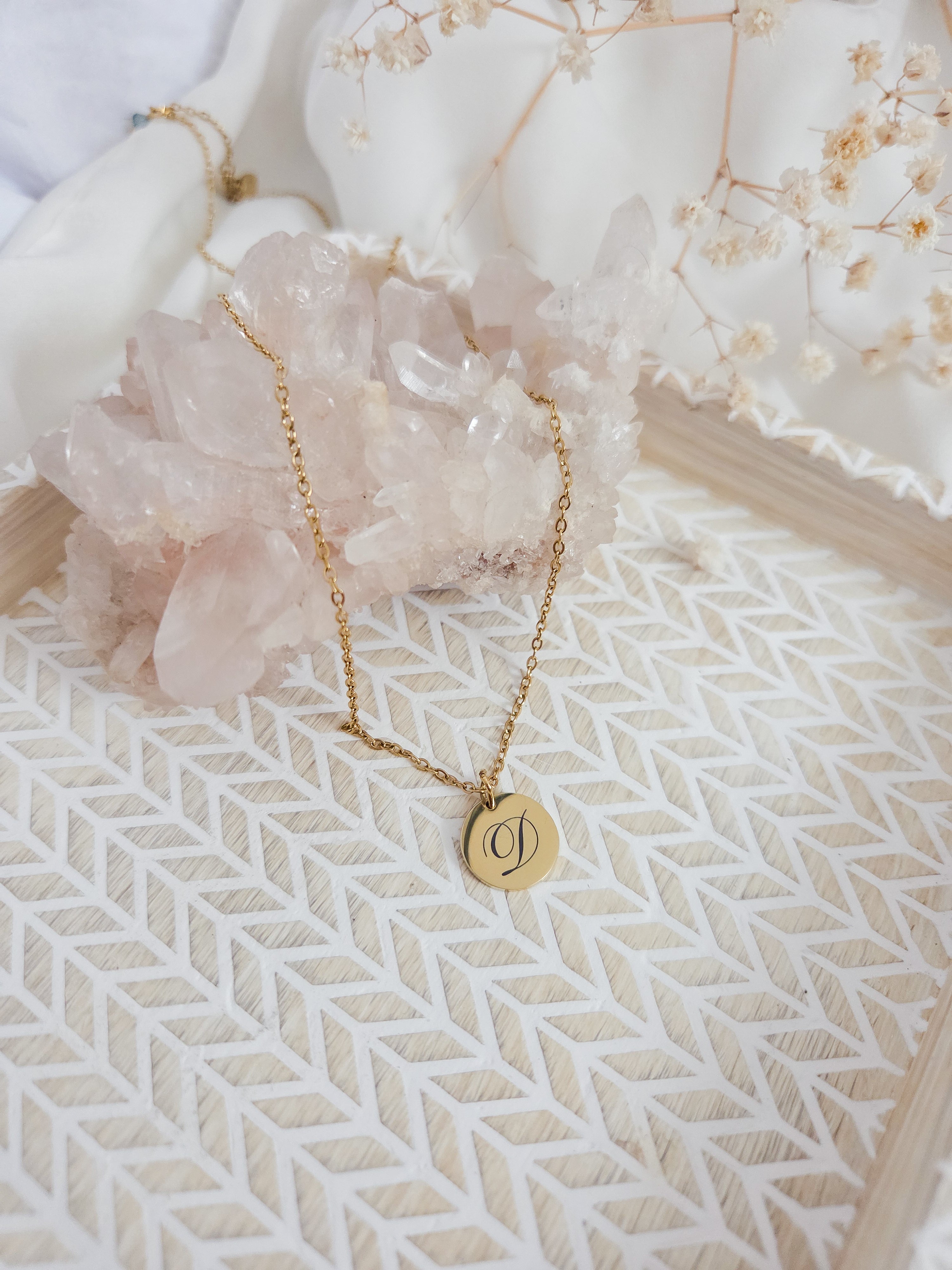 Gold necklace with a round pendant on a textured surface with crystals and flowers in the background