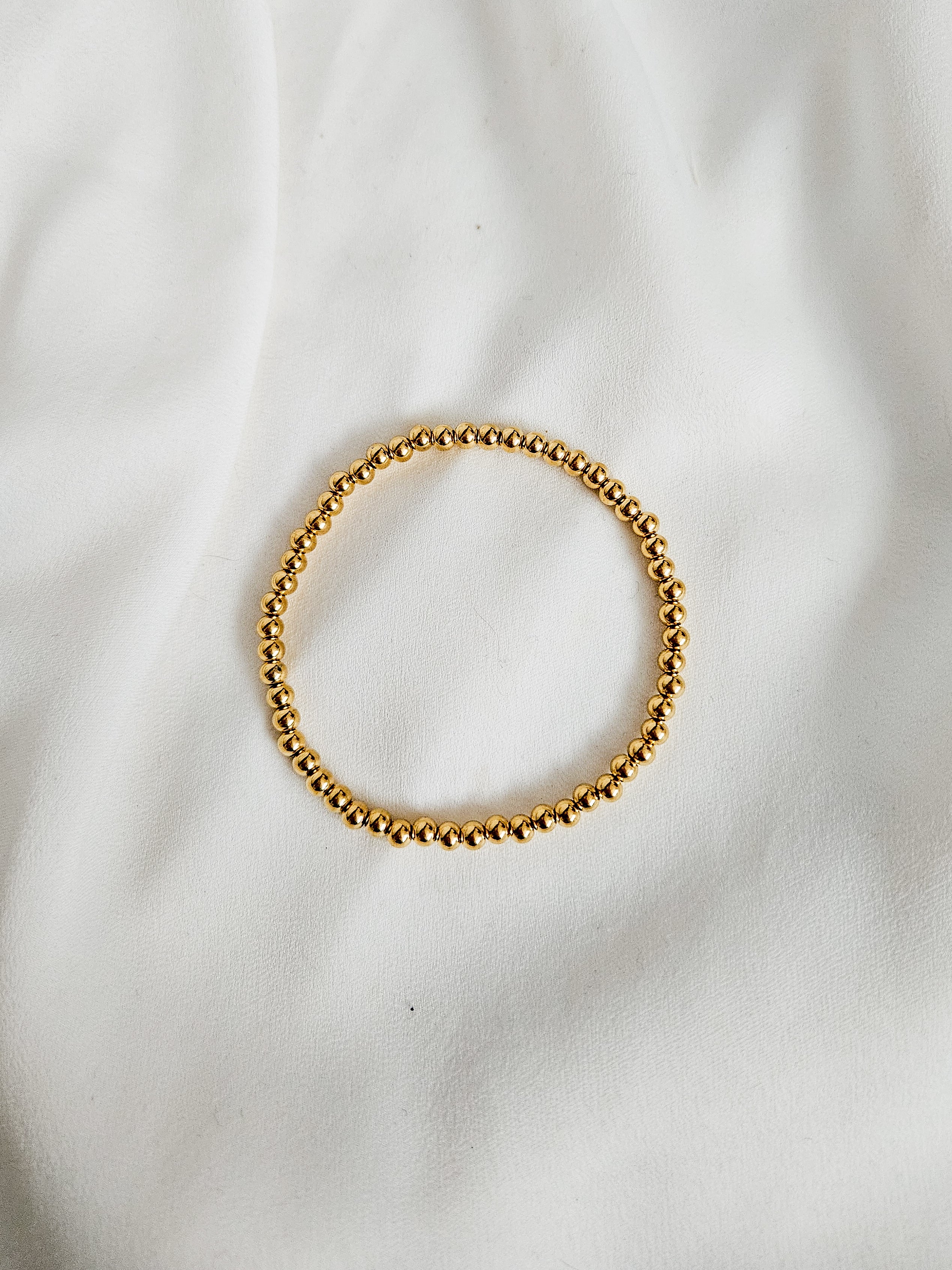 Handmade, gold, waterproof beaded bracelet on a white fabric background.