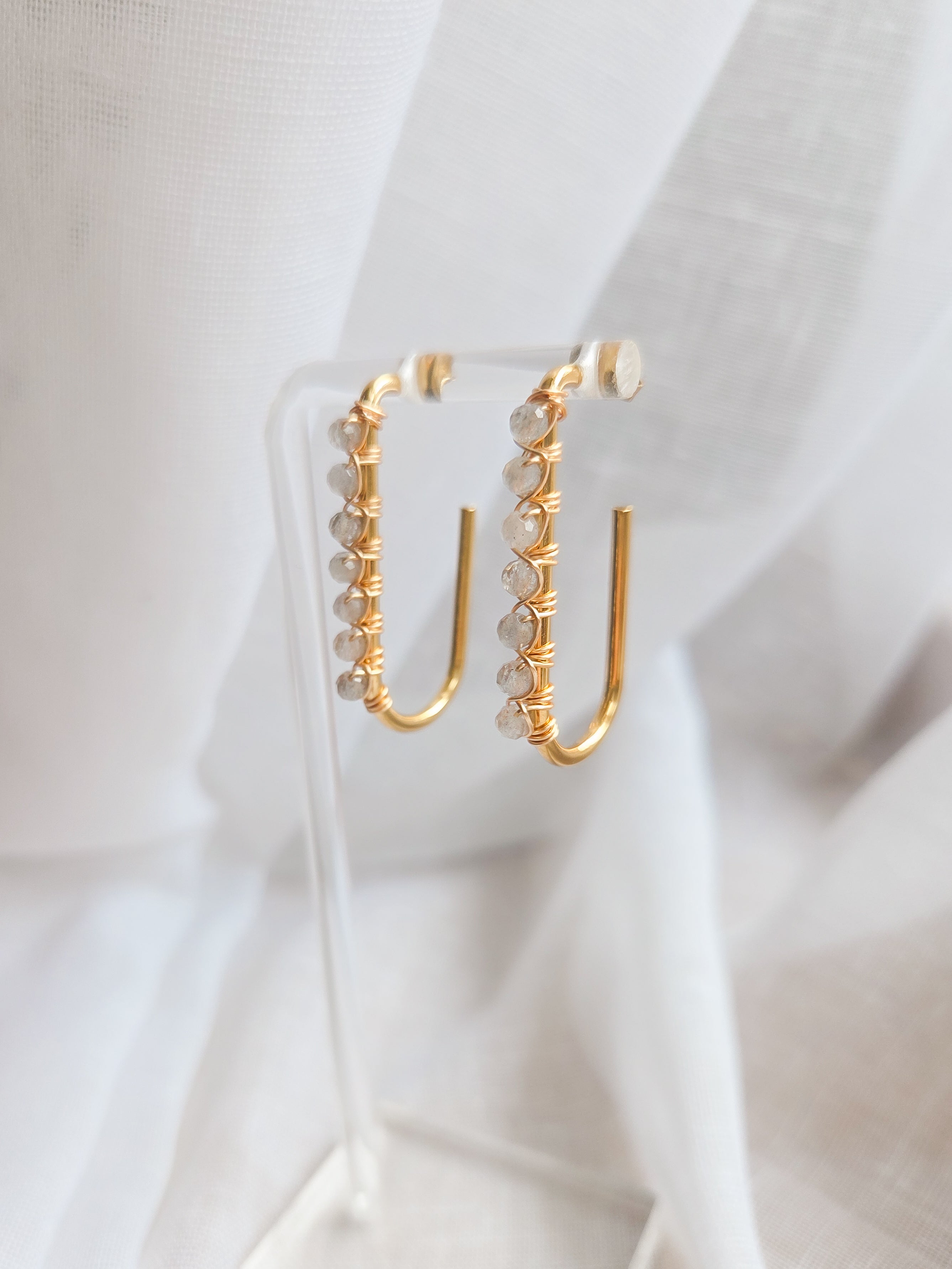 Gold hoop earrings with labradorite gemstone beads on a white fabric background