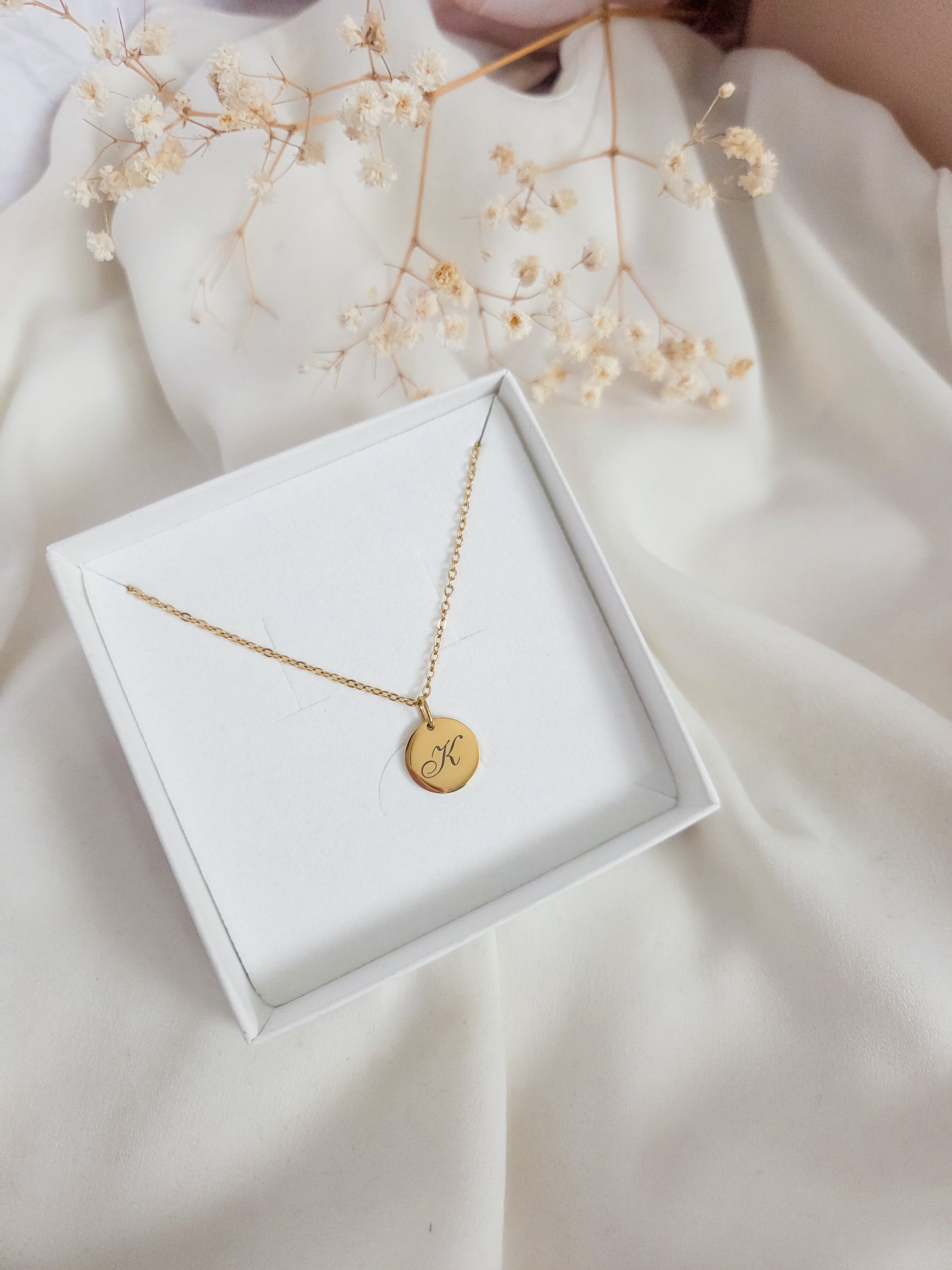 Gold necklace with a round pendant in a white jewelry box on a light fabric background
