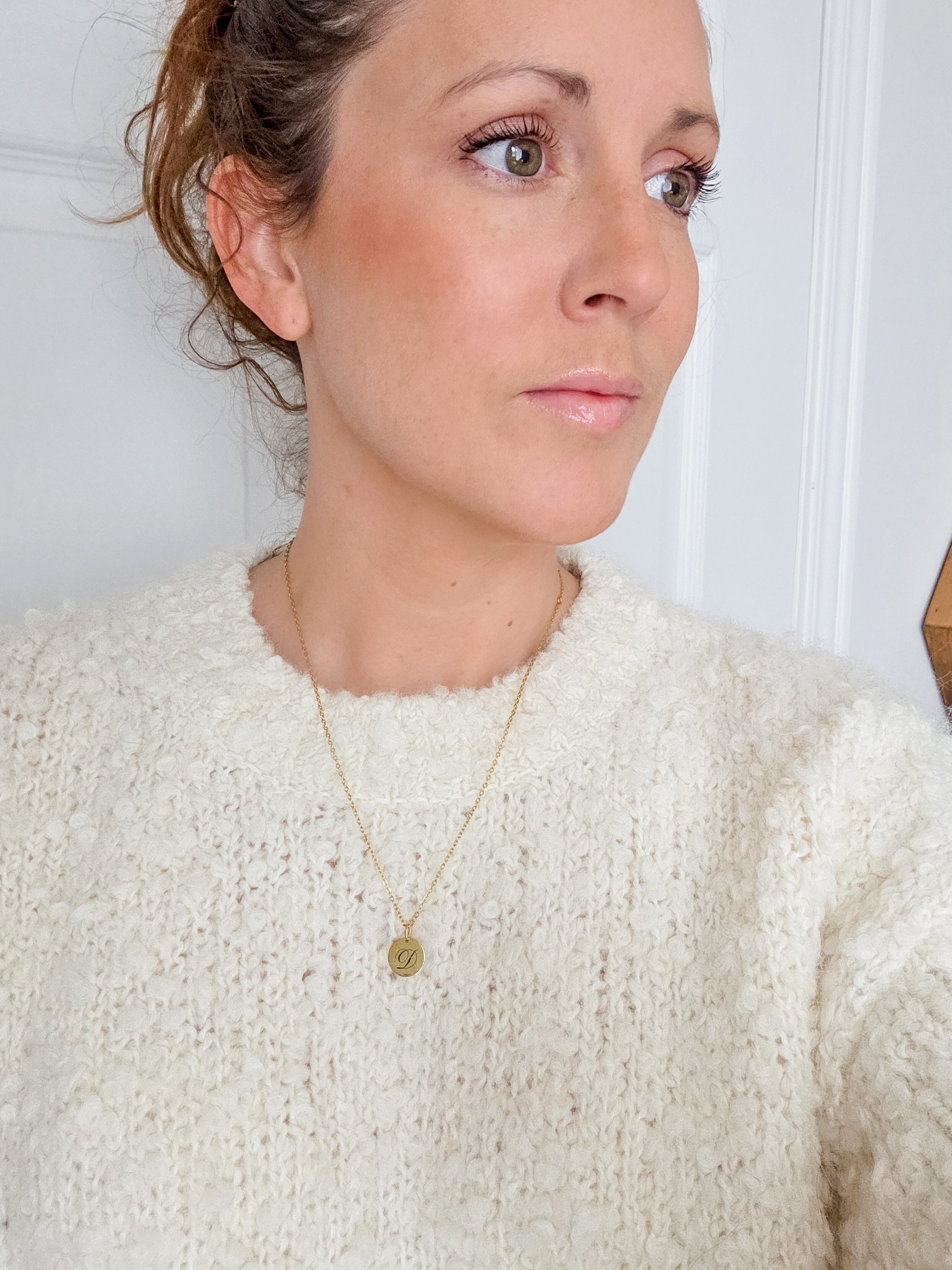 Woman wearing a white sweater and gold necklace against a plain background