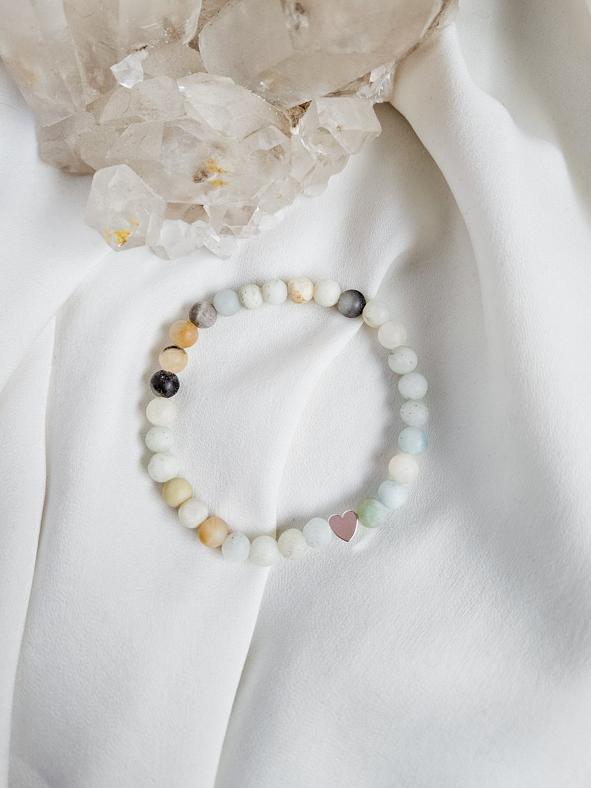 Multicolored amazonite beaded bracelet on a white fabric background with crystals.
