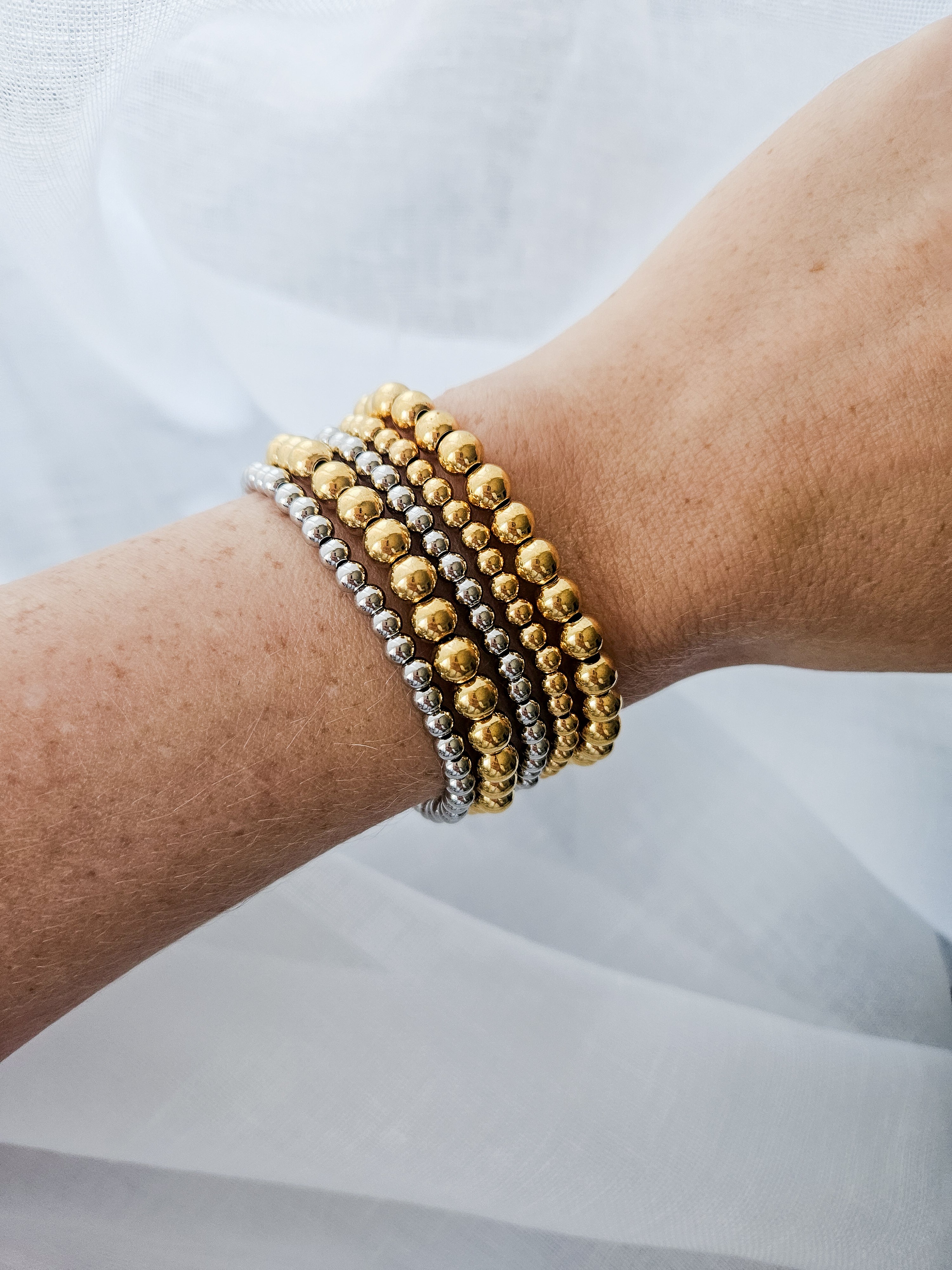Gold and silver beaded, tarnish proof, stretch bracelets worn stacked on wrist.