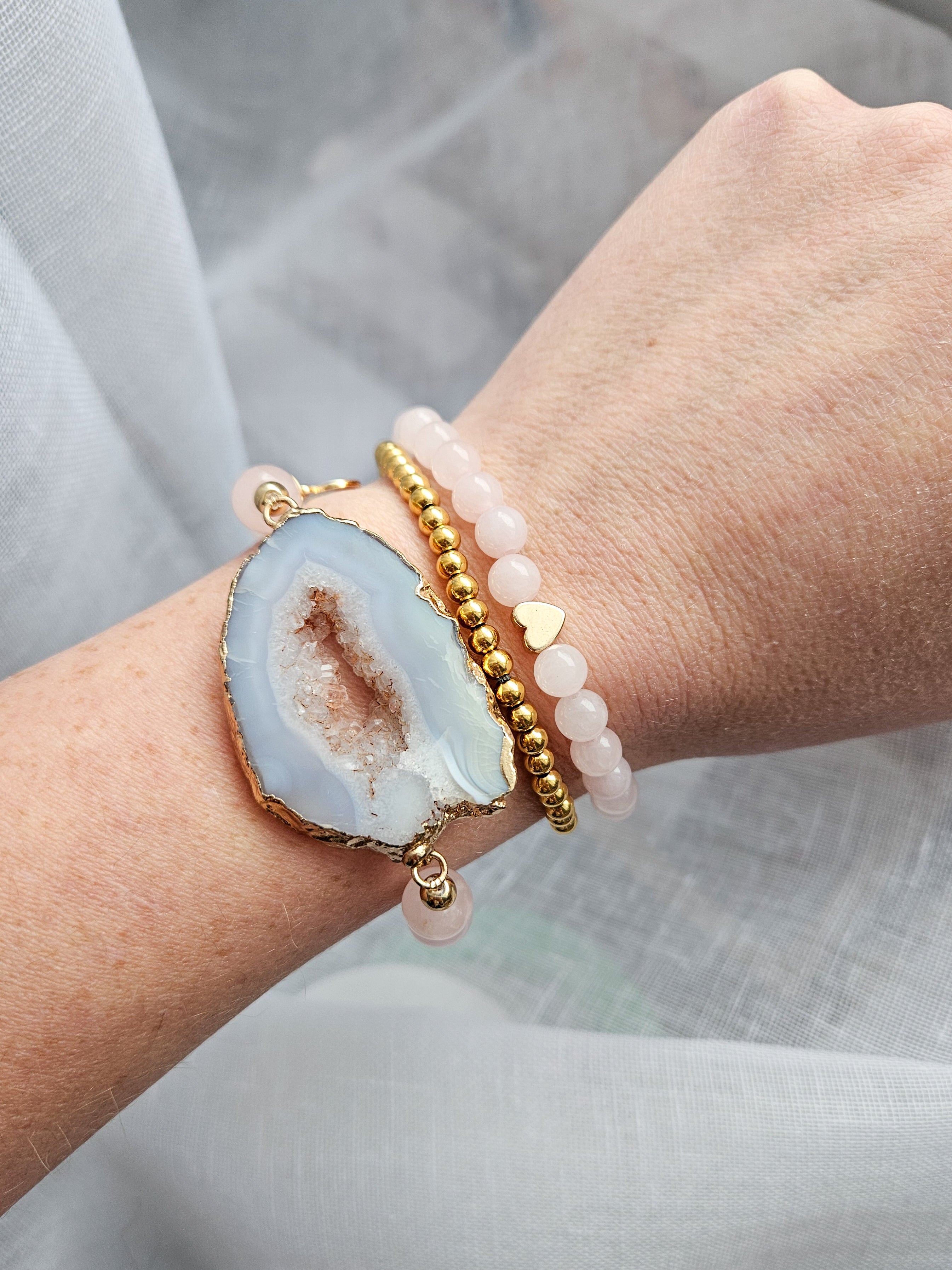 Close-up of a wrist wearing a bracelet with a natural agate geode stone design and two other bracelets on a light background